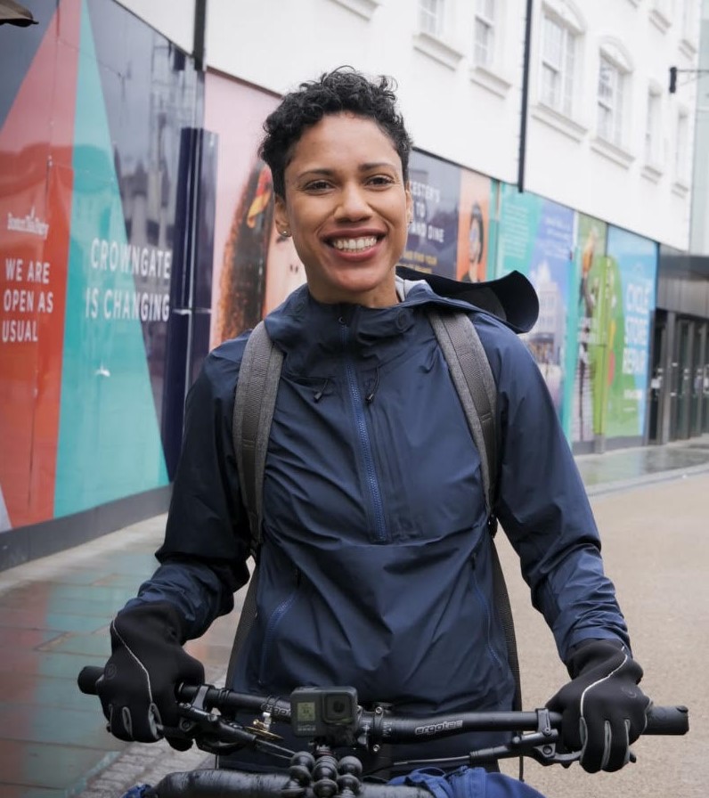 A close-up photo of Dulce standing on a high street and holding a bike with a Go-Pro camera attached to the handlebar.