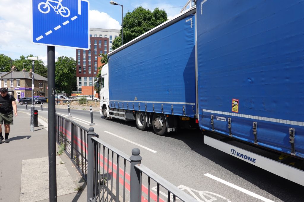 Photo shows an extended HGV lorry cutting a corner containing a cycle lane that is paint-based at that point (there are bollards further along). There is also guard railing.
