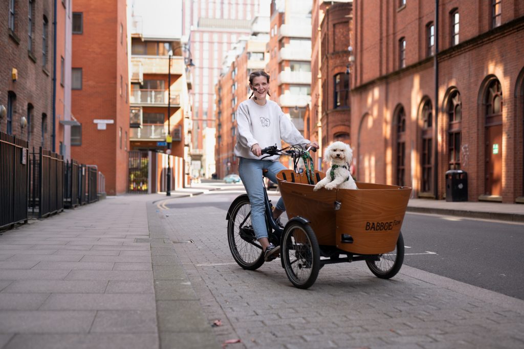 Photo of Harrie Larrington-Spencer riding a cargo trike with Frida the dog in the basket.