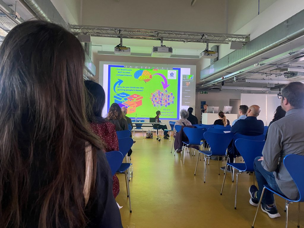 Picture of a room with attendees and a presenter at the front (Jean Hewitt) speaking to slides.