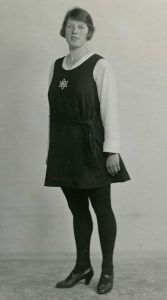 Black & white photograph of a woman wearing a 1920s gym dress with block stockings and heeled shoes
