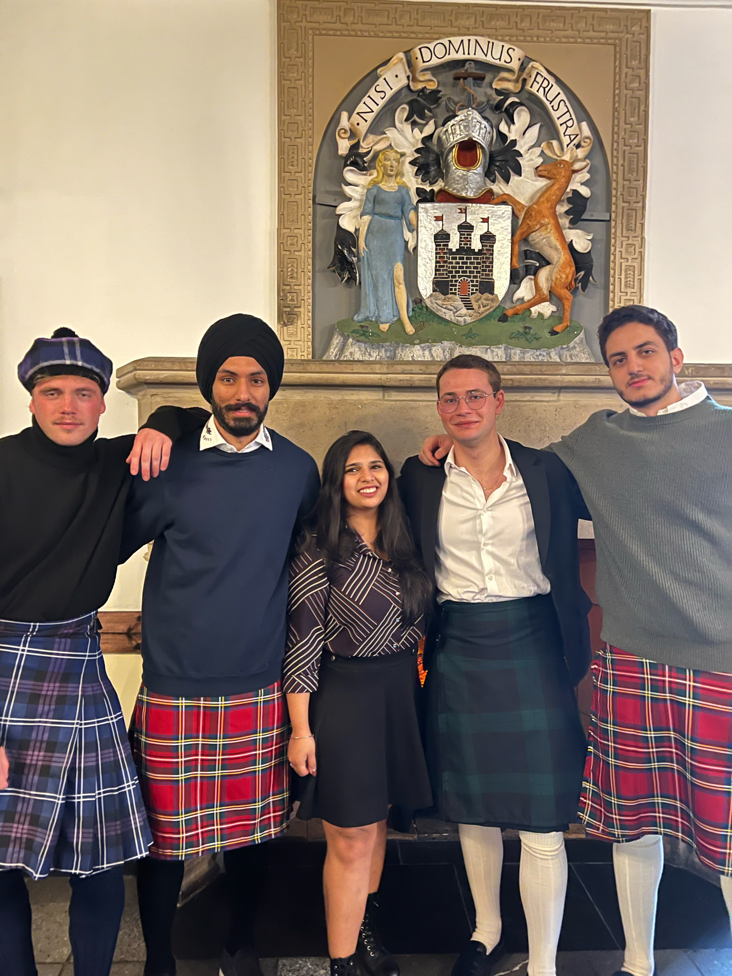 Students gathered in front of the mantelpiece wearing kilts