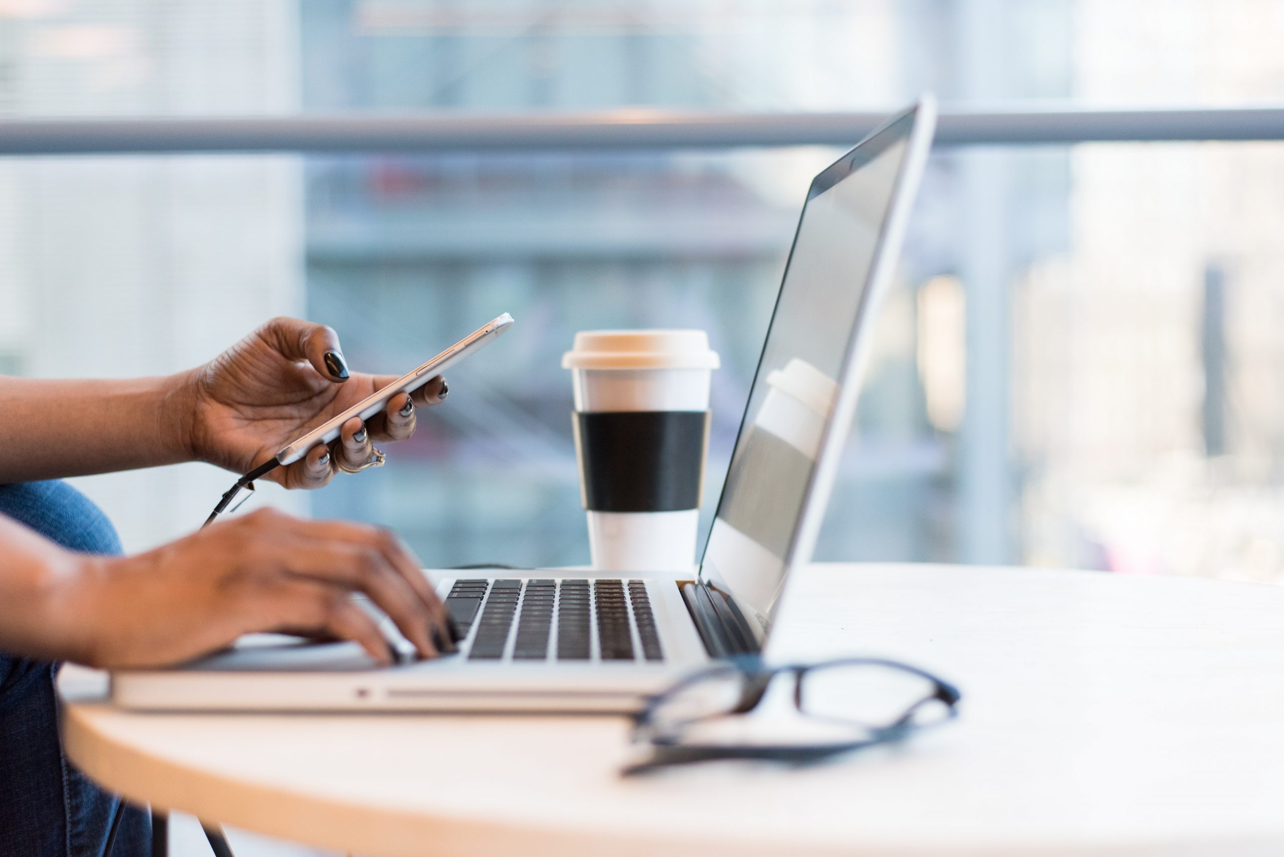 person using smartphone and Macbook in office with takeaway Coffee