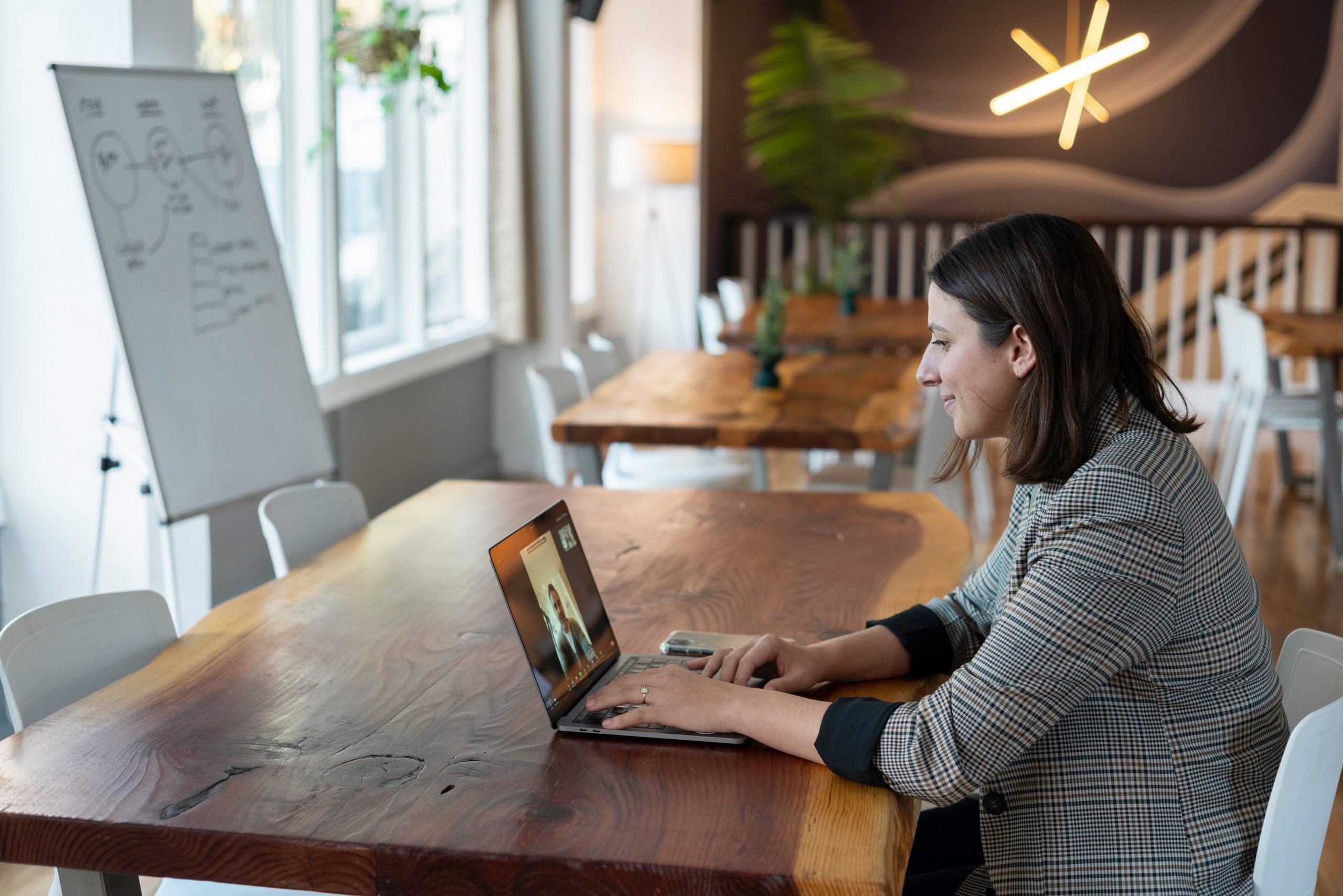 A salesperson working in an office on a virtual call: woman in gray and white striped long sleeve shirt using silver macbook