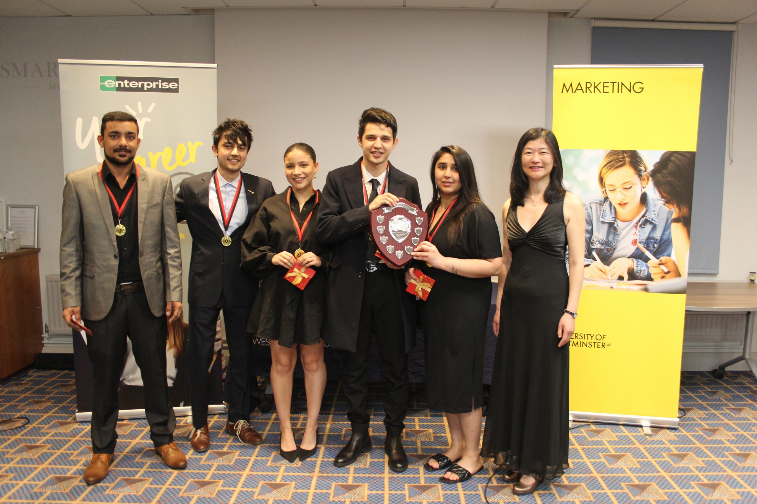 Prize-Giving Ceremony with winning team and Donna Mai flanked by Marketing and Enterprise banners