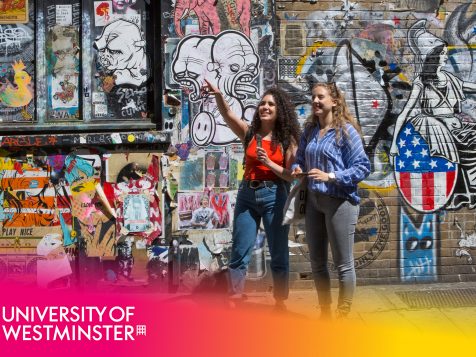 Two female students exploring London in front of a graffitied wall