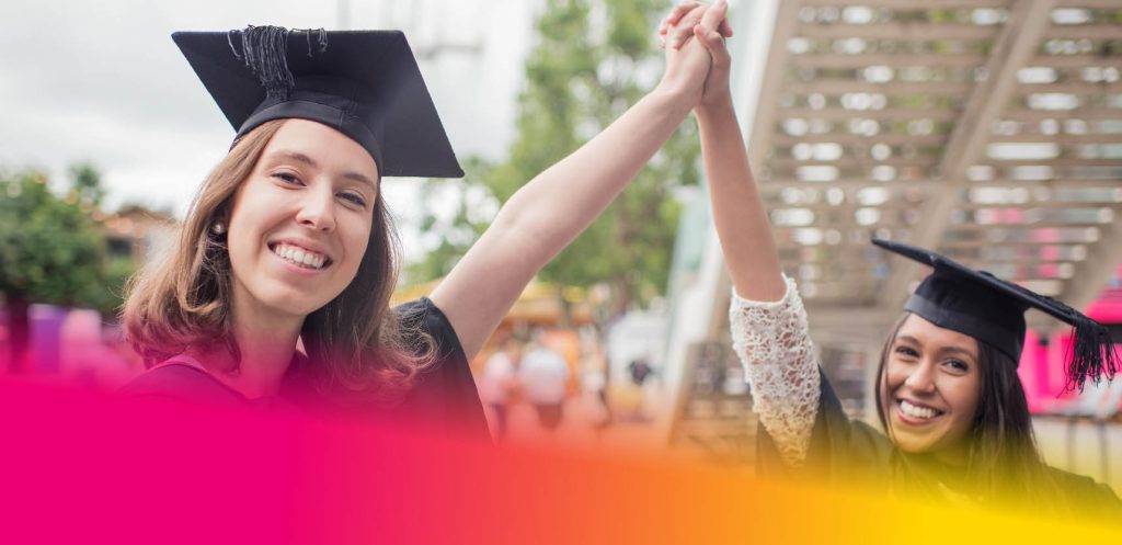 Two female students in graduation gowns and mortar boards celebrating