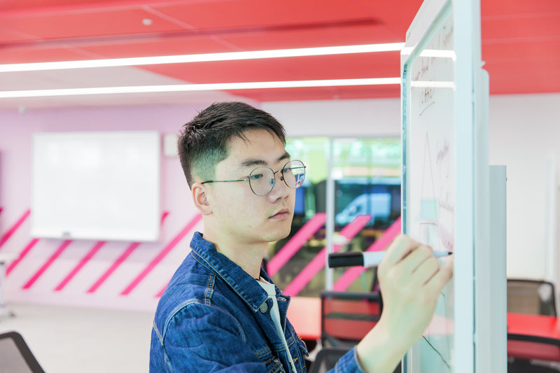 male-student-writing-on-whiteboard-pink-neon-background