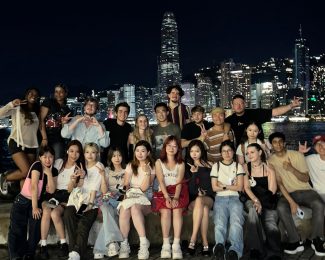 A group of people posing for a photograph in front of the Hong Kong skyline at night