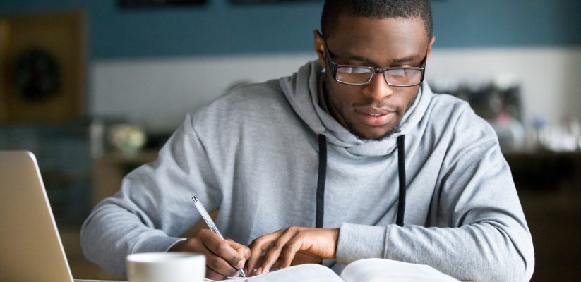 Man sitting at laptop with a coffee taking notes