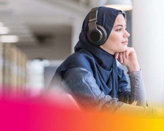 Female student wearing headphones looking out of the library window.