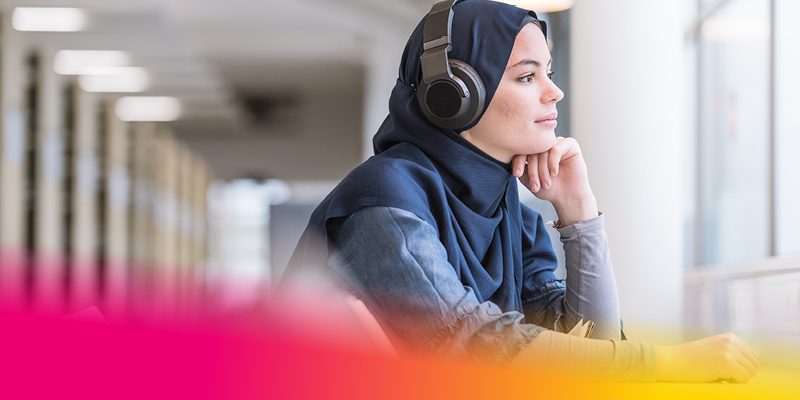 Female student wearing headphones looking out of the library window.