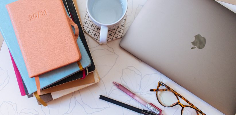 An aerial image of a mug, laptop, notebooks, pens and glasses on a desk