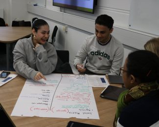 A group of 4 students making notes for a project, talking and laughing