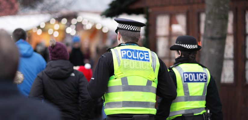 photo of a male annd female police officer from behind, walking through a busy crowd