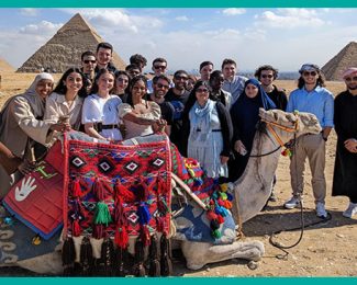 WWC Cairo group with camel in front of the Pyramids-teal border-Westminster Working Cultures Cairo-Argia Hernandez Ochoteco