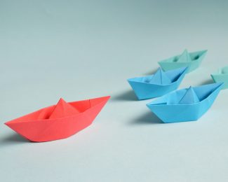 Red, blue and green paper boats - the red boat is leading the rest