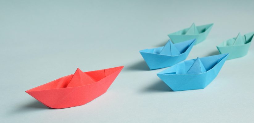 Red, blue and green paper boats - the red boat is leading the rest