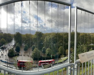 A panoramic vista of London from the top of the Marble Arch Mound with an iconic London Red Double-Decker bus in shot.